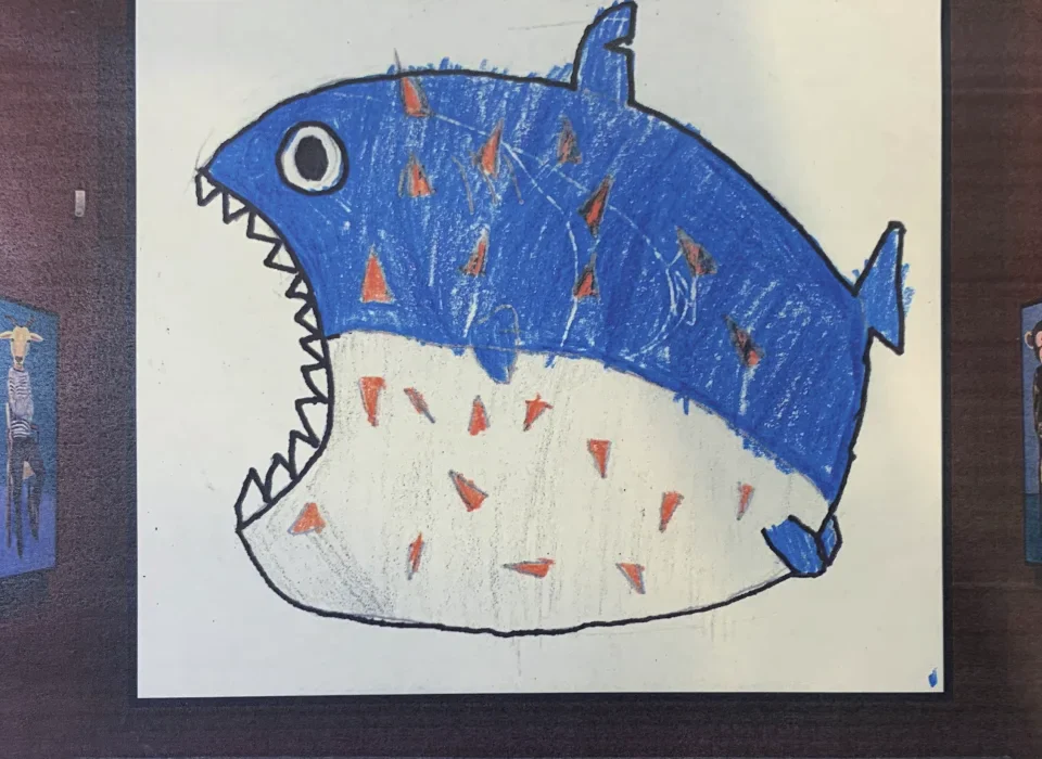 A child's blue fish character drawing hung on a wall like a framed exhibit