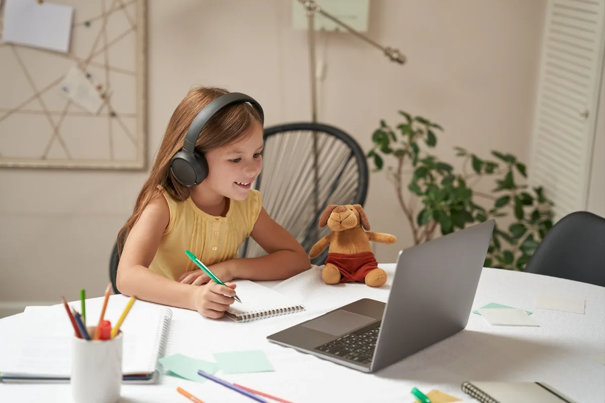 A child wearing headphones writing in a notebook
