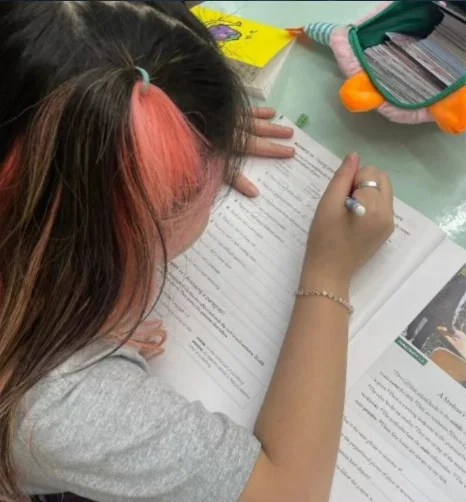 Overhead view of a student writing with a pen over a textbook with an English passage