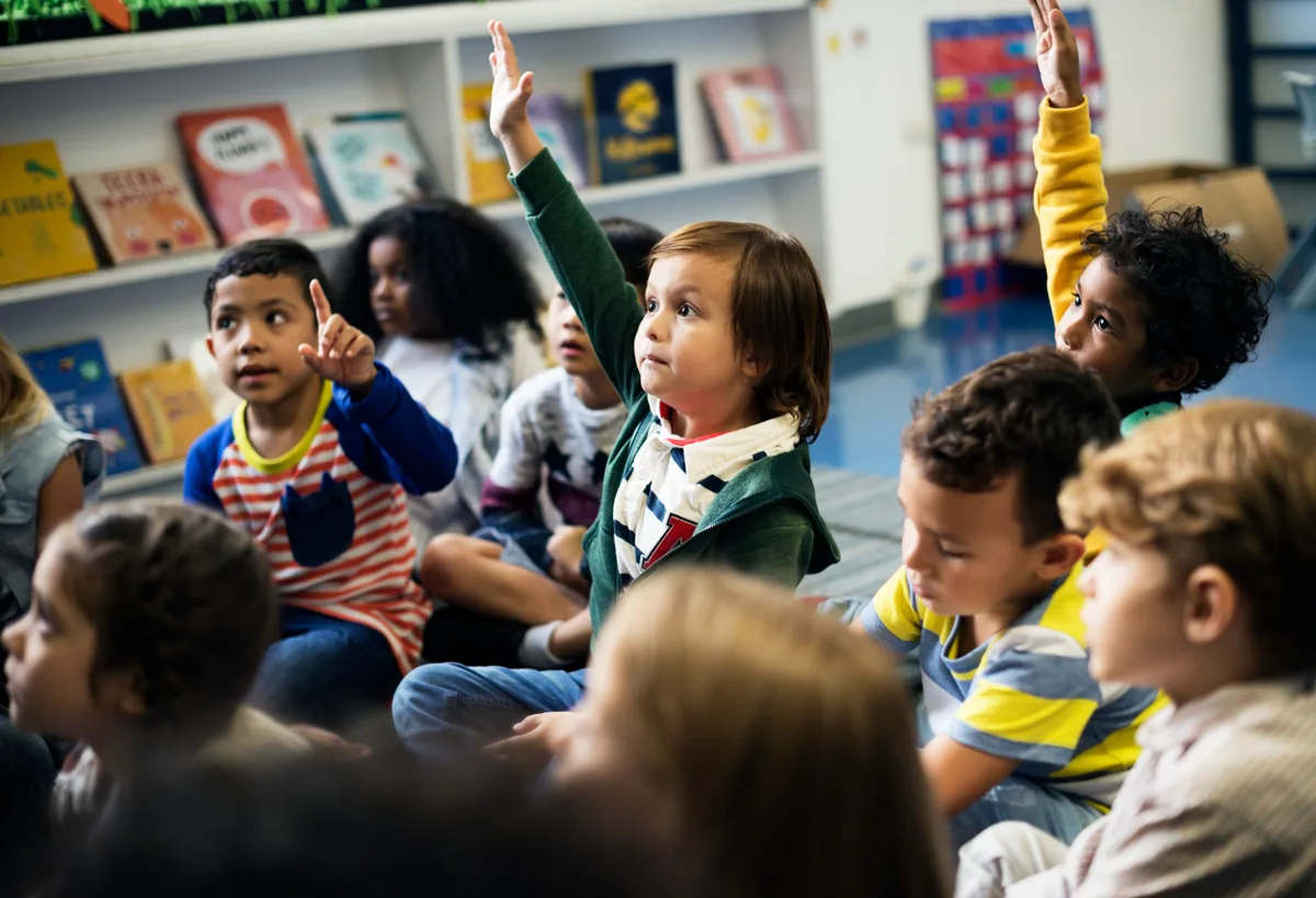 Children raising their hands in front of a picture-book shelf