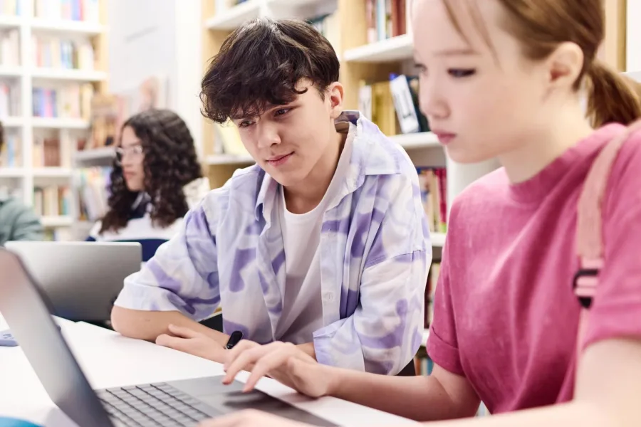 Teenagers looking at a laptop together at a library desk