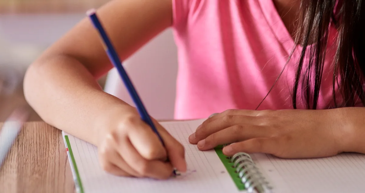 A child's hand writing in a notebook with a pencil